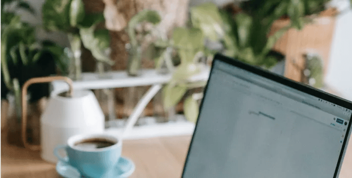 Laptop sitting on a table by a cup of coffee