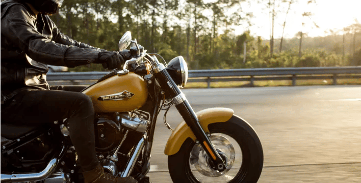 Side view of a person riding a yellow motorcycle down the road.