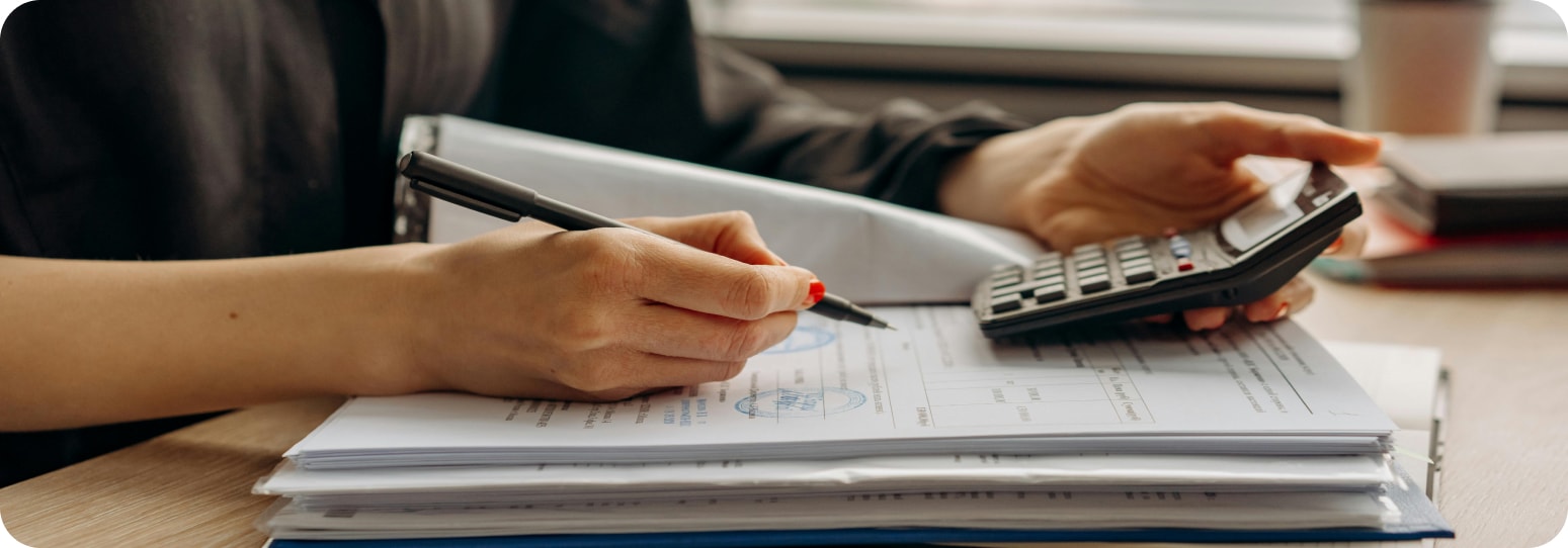 Woman holding a calculator in one hand and a pen in another on an open book